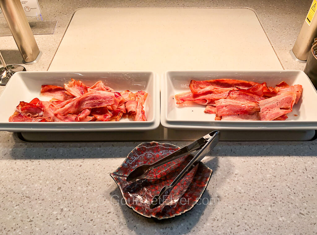 Two serving dishes containing bacon are placed side by side on a counter.