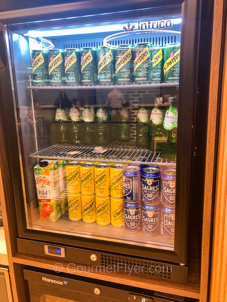 A refrigerator with a glass door contains 3 shelves of canned and bottled drinks.