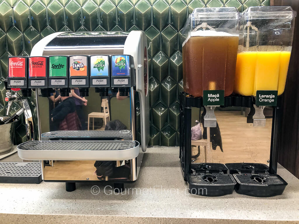 A soda machine with 6 taps is accompanied by two tall juice dispensers on the right.