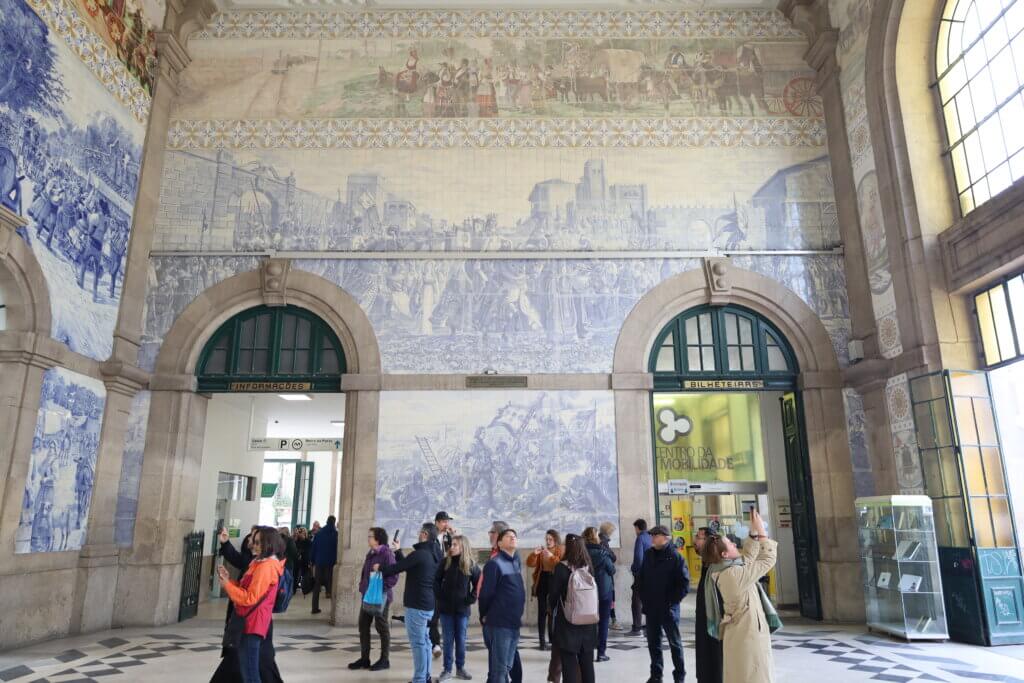 Visitors are admiring the murals on the walls of a train station, taking pictures with their phones.