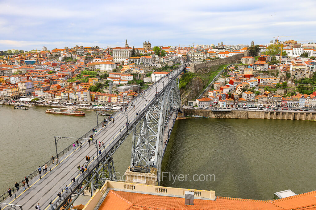 People are walking on the upper deck of a bridge which spans across a river to the city of Porto.