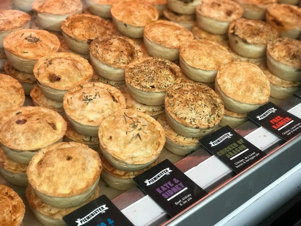 Rows of small round British pot pies are stacked two high on a counter with labels.