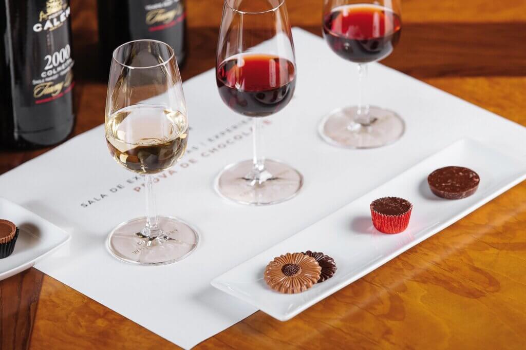Three glasses of different wines are displayed with their respective bottles and paired with chocolate.