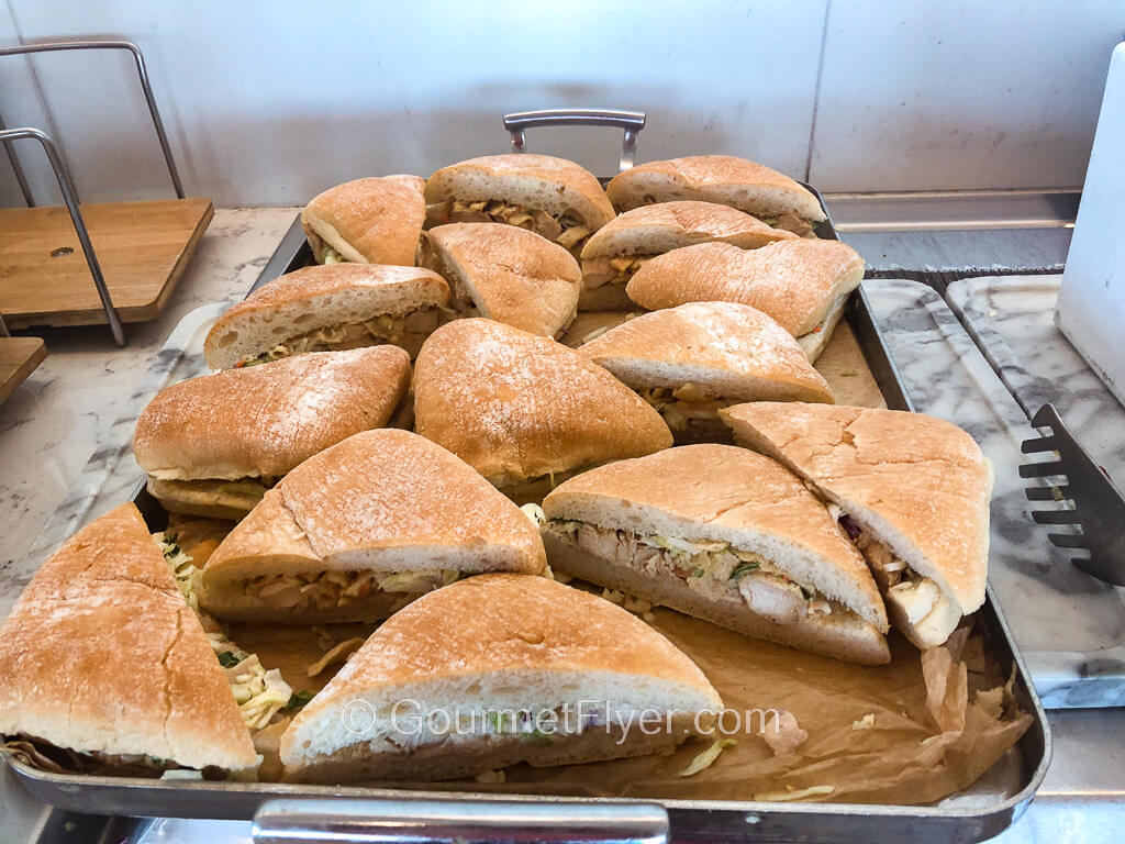 Sandwiches cut up in triangular shaped ciabatta breads are served in a silver tray.