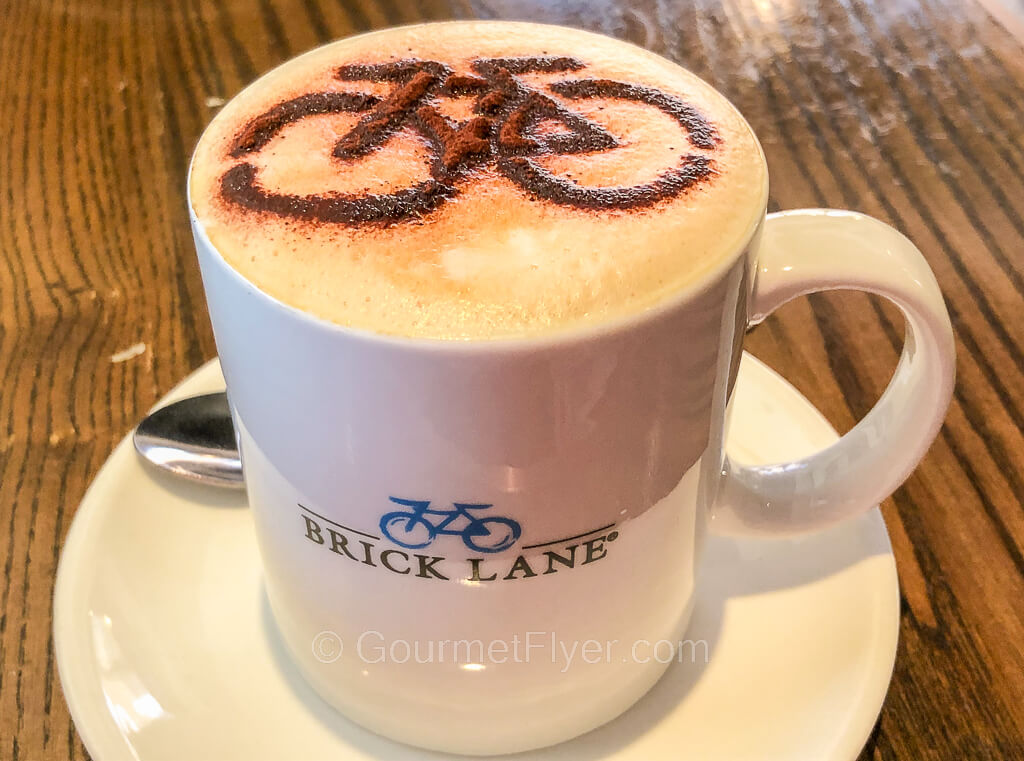 A coffee drink with a bicycle latte art on top is served in a mug.