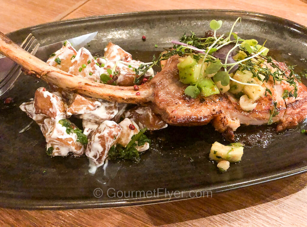 A tomahawk pork chop is served on a platter accompanied by potato salad.