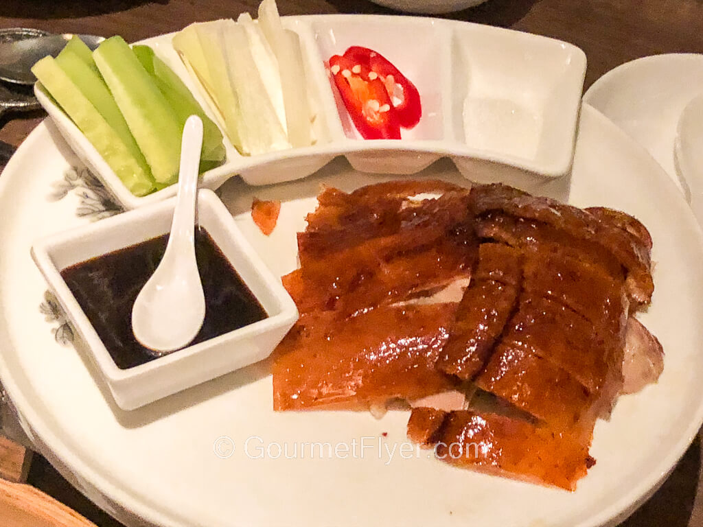 Sliced duck meat is served on a platter skin up with garnishments and a dark sauce.