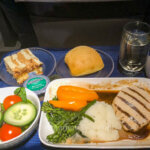 Review of United's First Class flight features a dinner set with chicken, side salad, cake for dessert, and a glass of red wine.