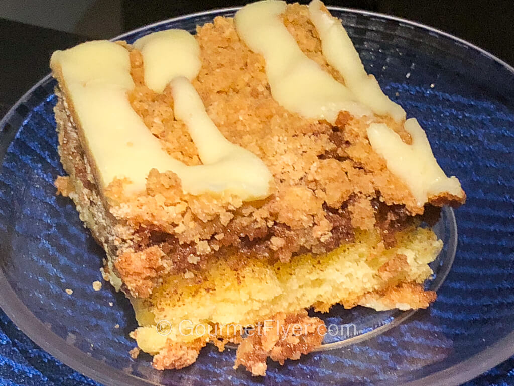 A square cut up of a cake is topped with brown crumbs and a yellow frosting.