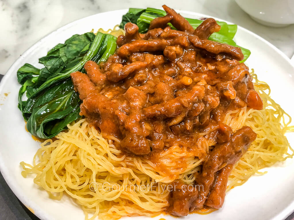 A plate of noodles is topped with a meat sauce and accompanied by a serving of Chinese vegetables.