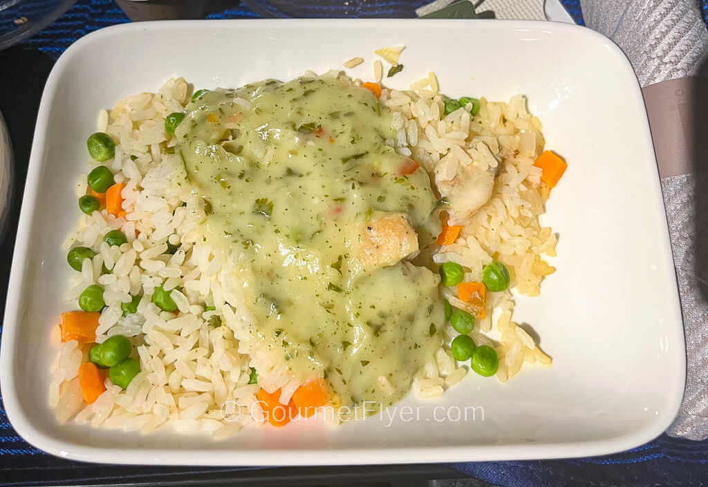 A plate of rice pilaf mixed with peas and carrots is covered with a green sauce served over a piece of chicken.