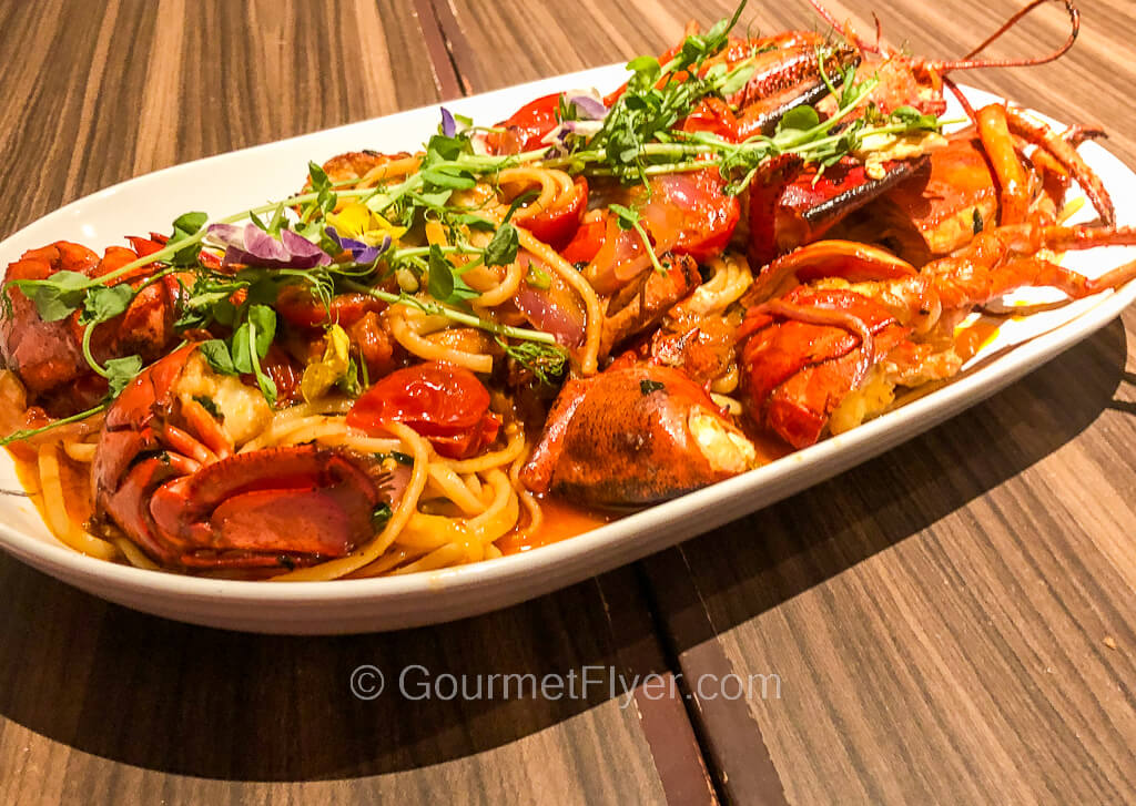 A cut-up whole lobster is served in a long platter along with spaghetti in a red sauce.