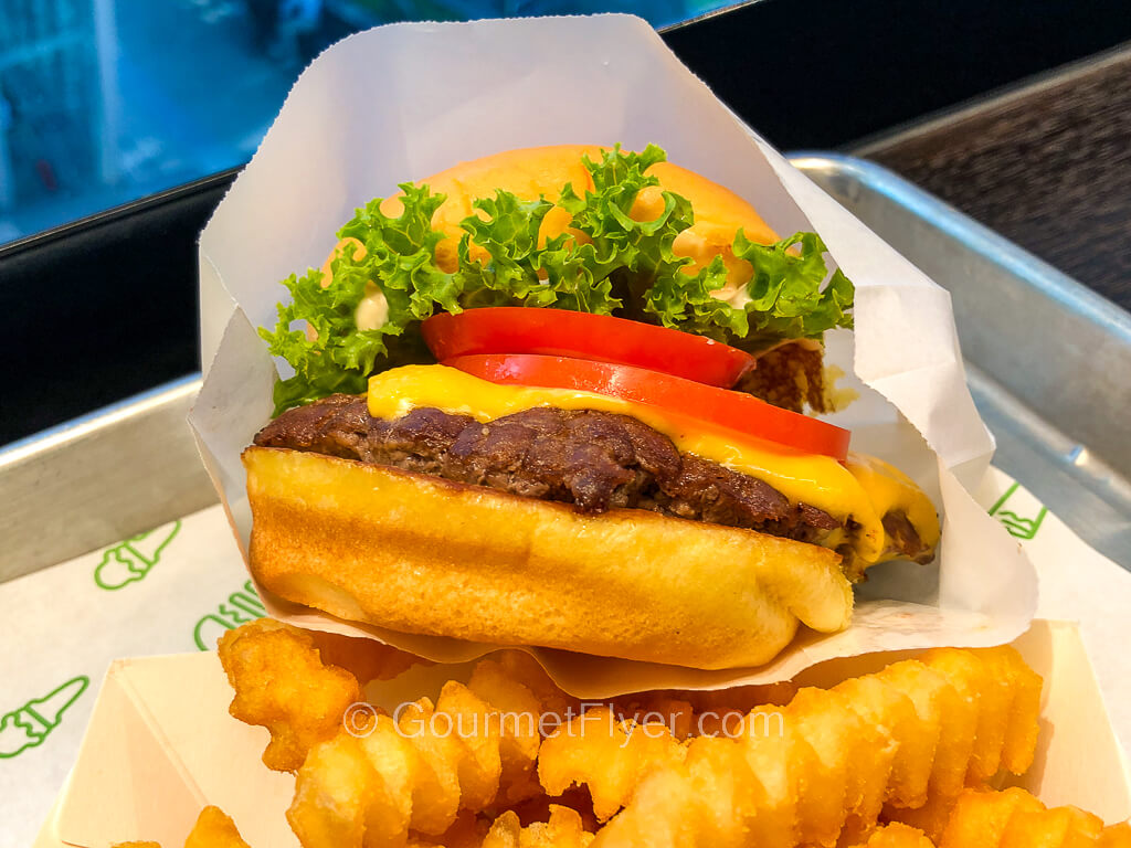 A cheeseburger topped with lettuce and tomato is accompanied by a side of crinkle cut fries.