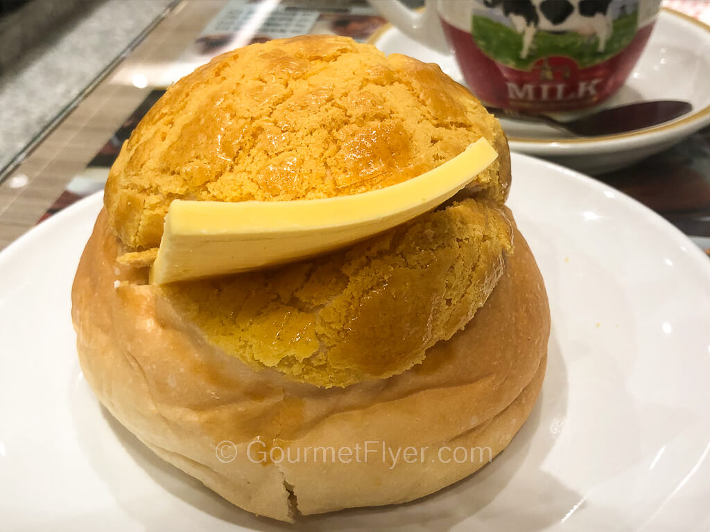 A pineapple bun is cut in the side with a slab of butter inserted into it.