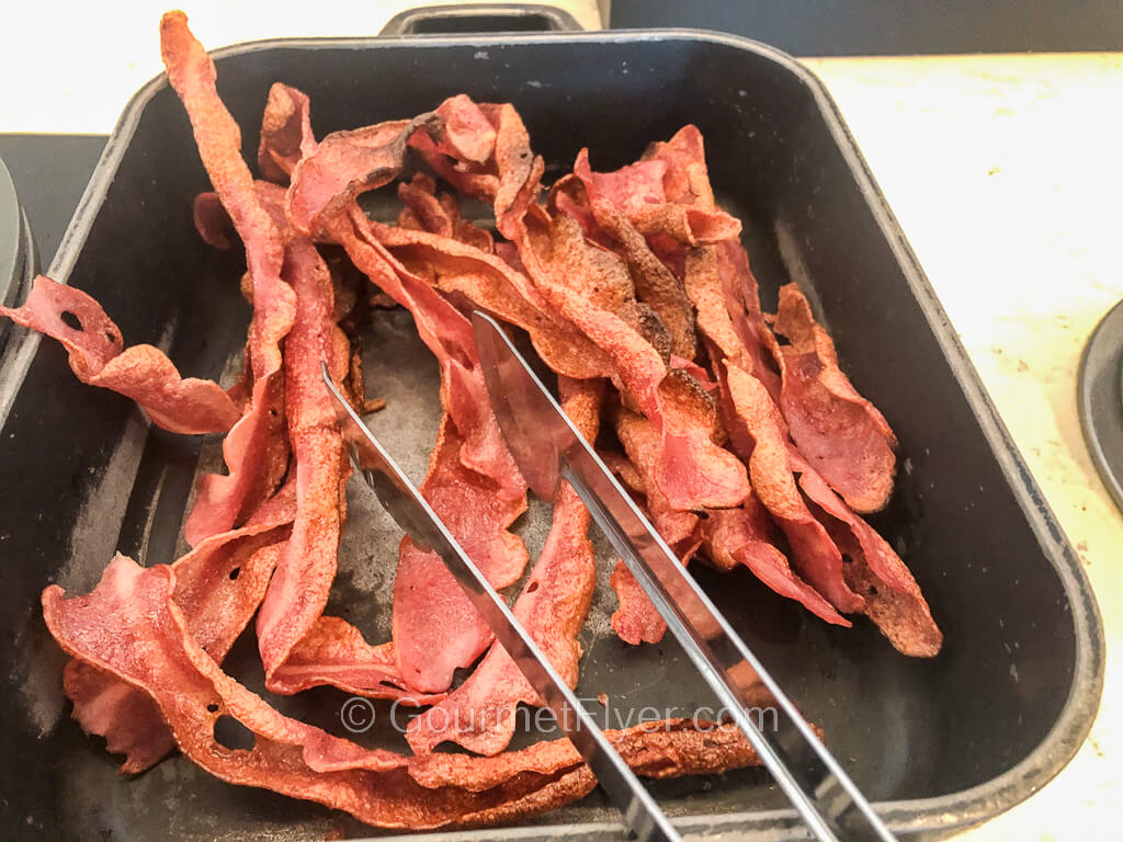 A long and heated platter contains pieces of fried crispy bacon.