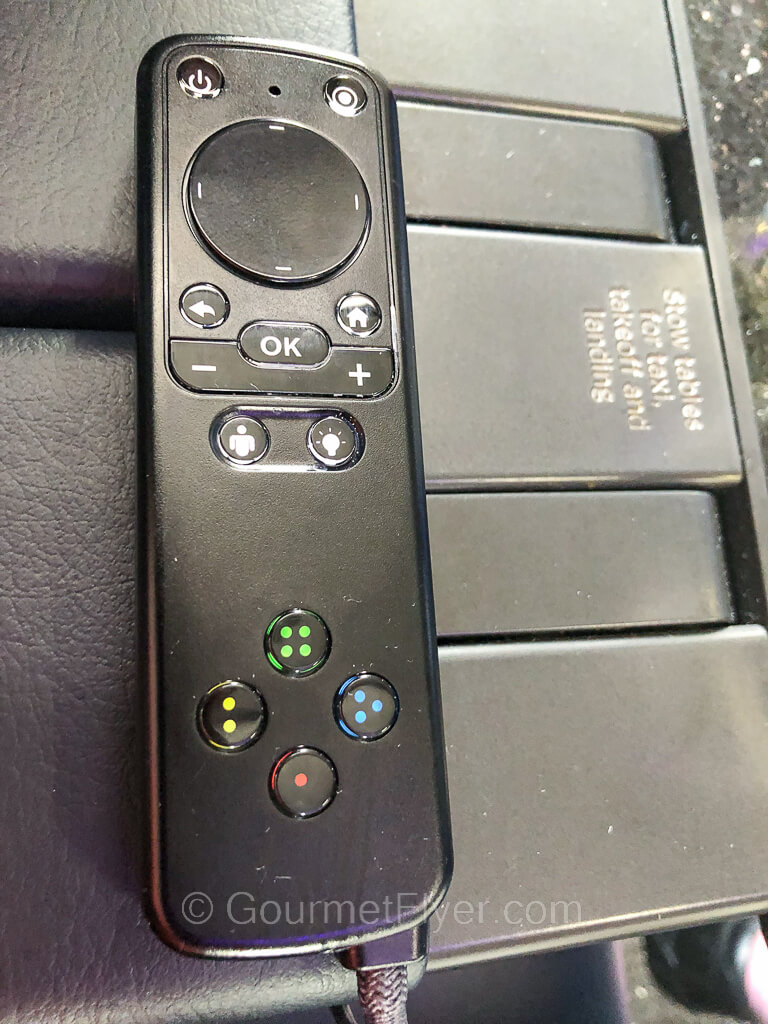 A remote control with many colorful buttons is placed on a wide armrest.
