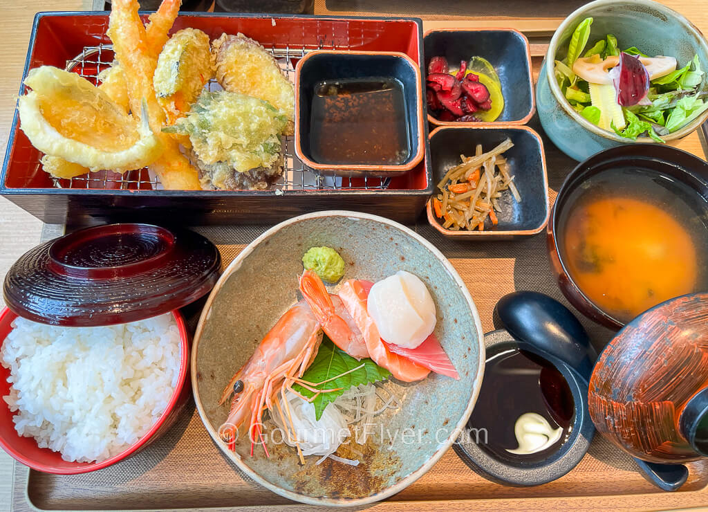 A Japanese set lunch with sashimi, fried shrimps, soup, salad, and rice served on a tray.