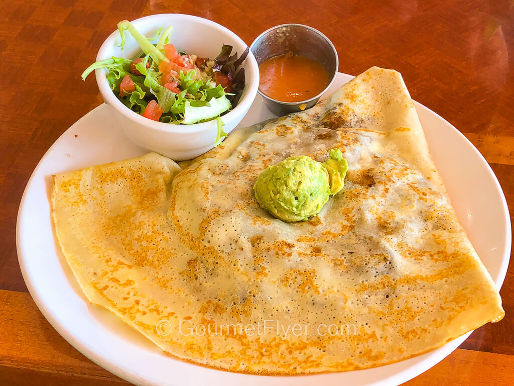 A folded triangular shaped crepe is topped with a small round scope of guacamole and accompanied by a small side salad.