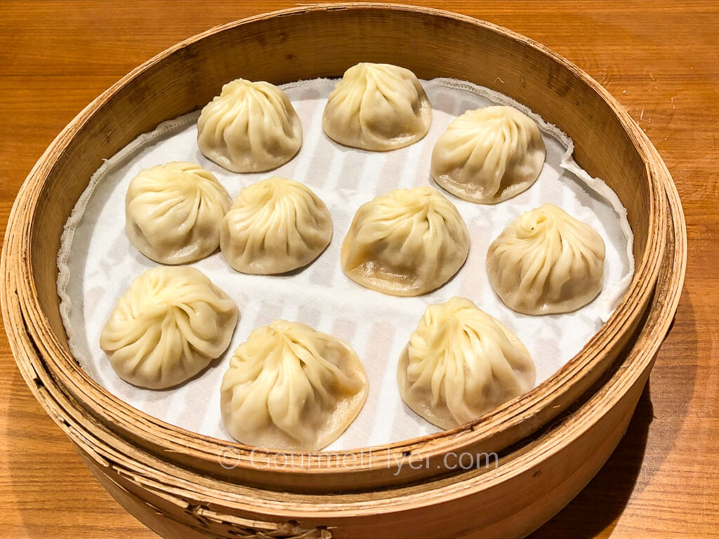 A bamboo basket contains 10 steamed dumplings placed on a white steam cloth.