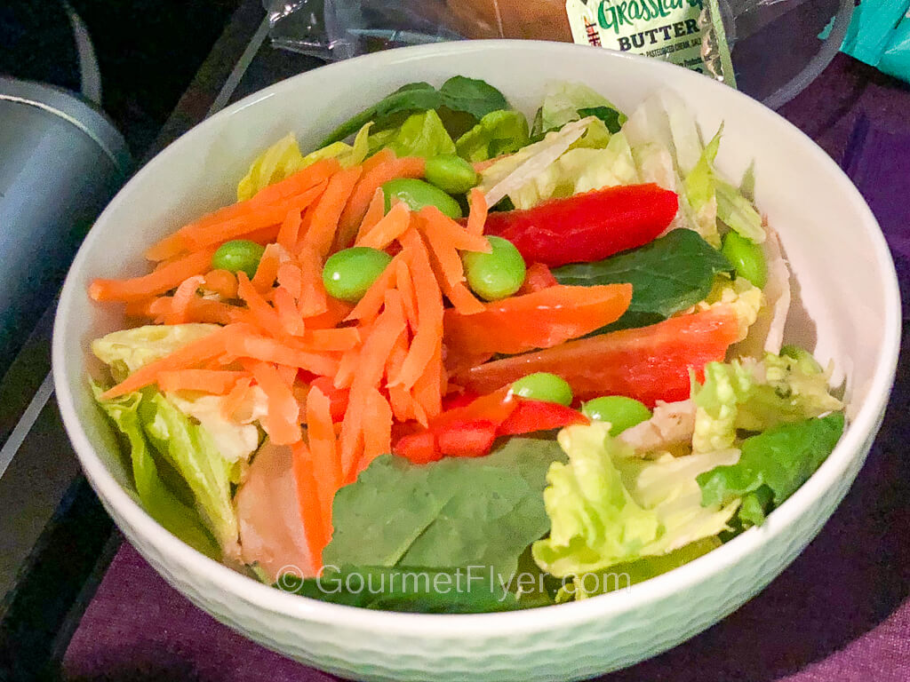A salad with lettuce and topped with colorful veggies is served in a white porcelain bowl on top of a dinner tray.