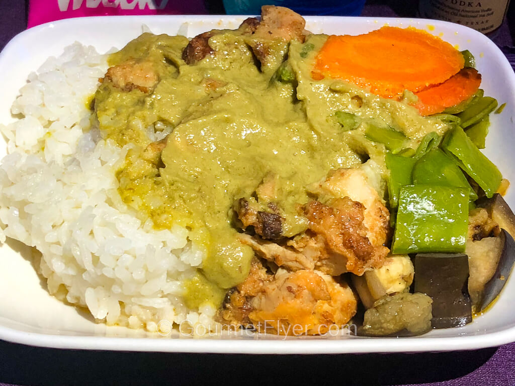 A plate of meat and white rice is covered with a thick green gravy and served with vegetables.