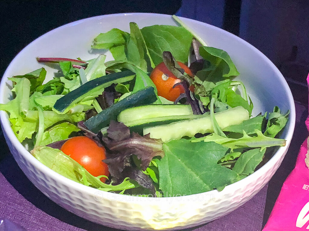 A green salad made with lettuce and a blend of vegetables is served in a white porcelain bowl.