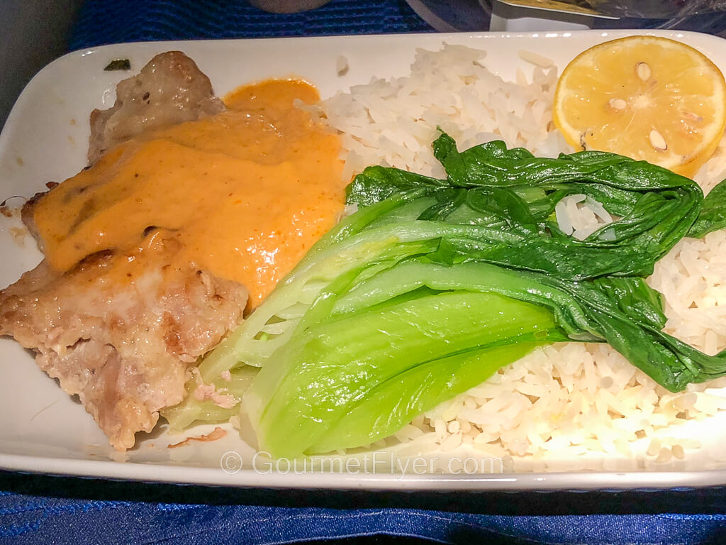 A piece of meat covered in a creamy yellow sauce is served with white rice and bok choy on a dish.