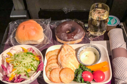 The food and beverage in United Airlines' Premium Plus class features a dinner tray with a chicken entree accompanied by a green salad, dessert, and a glass of white wine.
