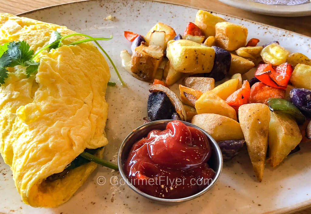 An omelet is accompanied by a serving of breakfast potatoes with ketchup on the side.