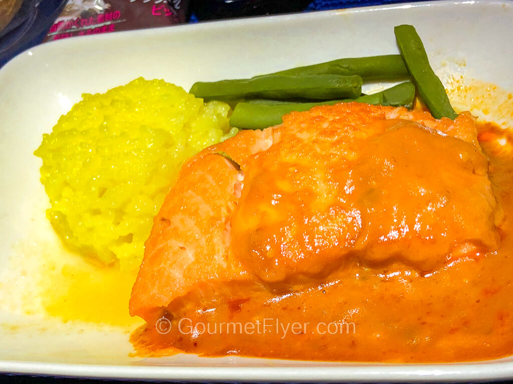 A thick slab of salmon is covered in a thick orange sauce and is accompanied by a ball of risotto.