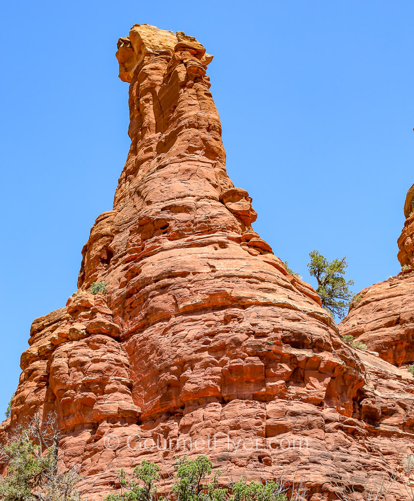 A spire-like red rock has a barrel like base and a narrow body.