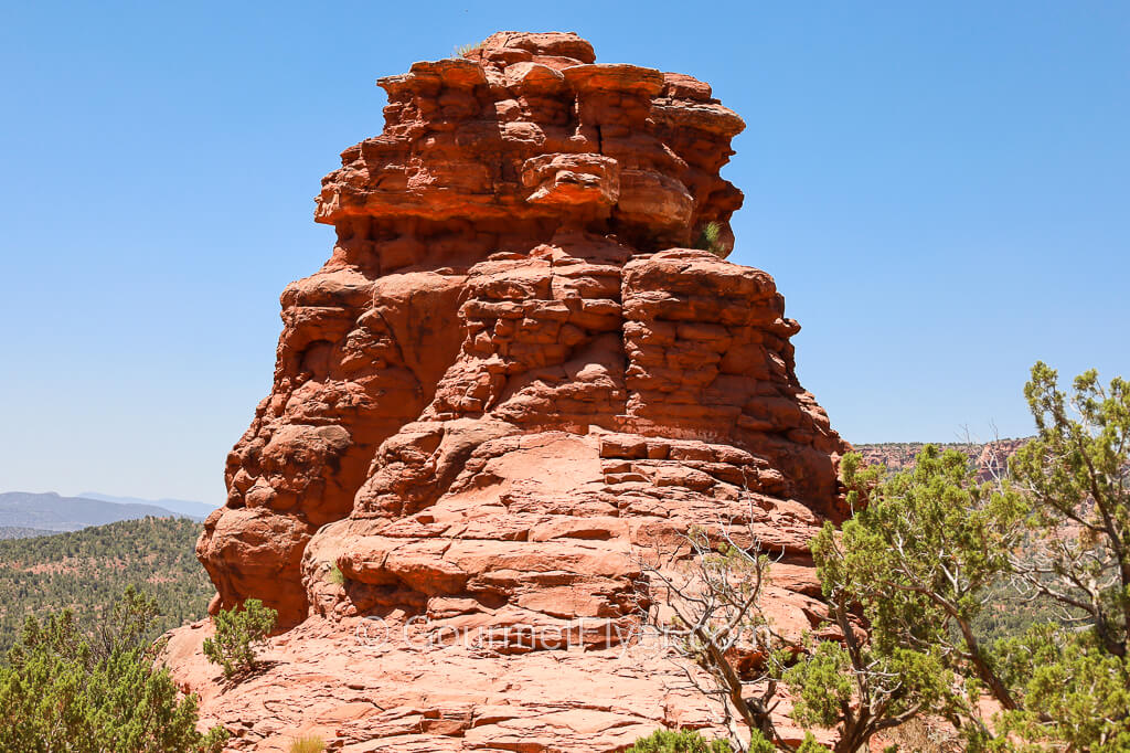 A mound-like red rock structure sits atop a hill under a sunny blue sky.