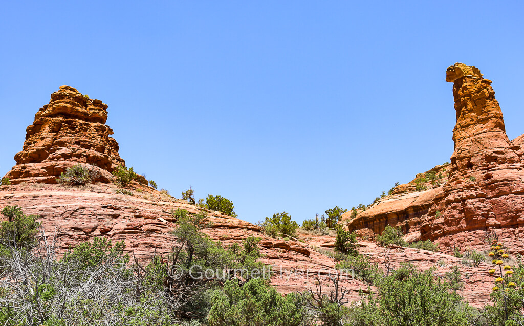 A space is between two red rock formations, a mound like on the left and a spire on the right.