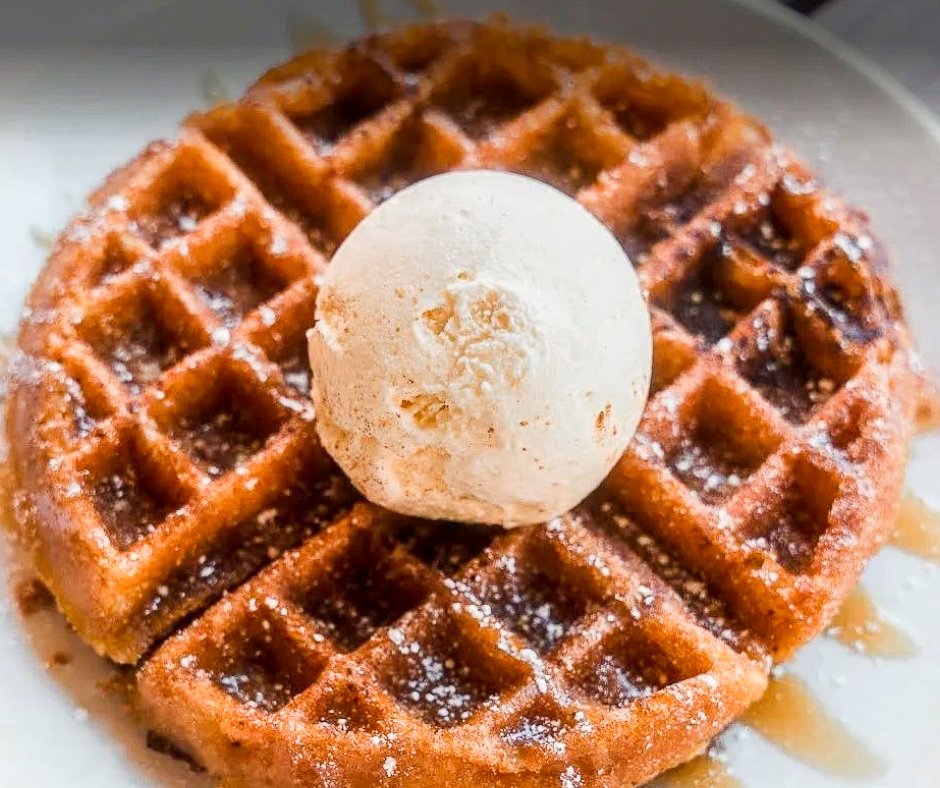 A toasted waffle is topped with syrup and a scoop of vanilla ice cream.