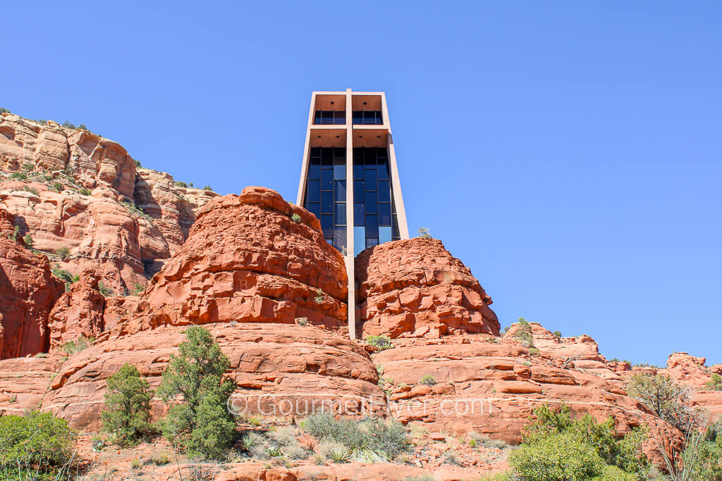 A tall rectangular structure with a cross sits atop a red rock formation.