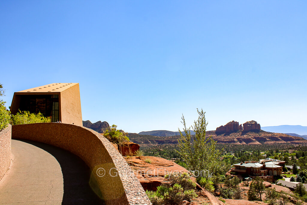 A curved and paved pathway has a scenery of red rock mountains to its right.