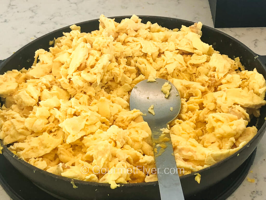 A large, round cast iron platter is filled with scrambled eggs.