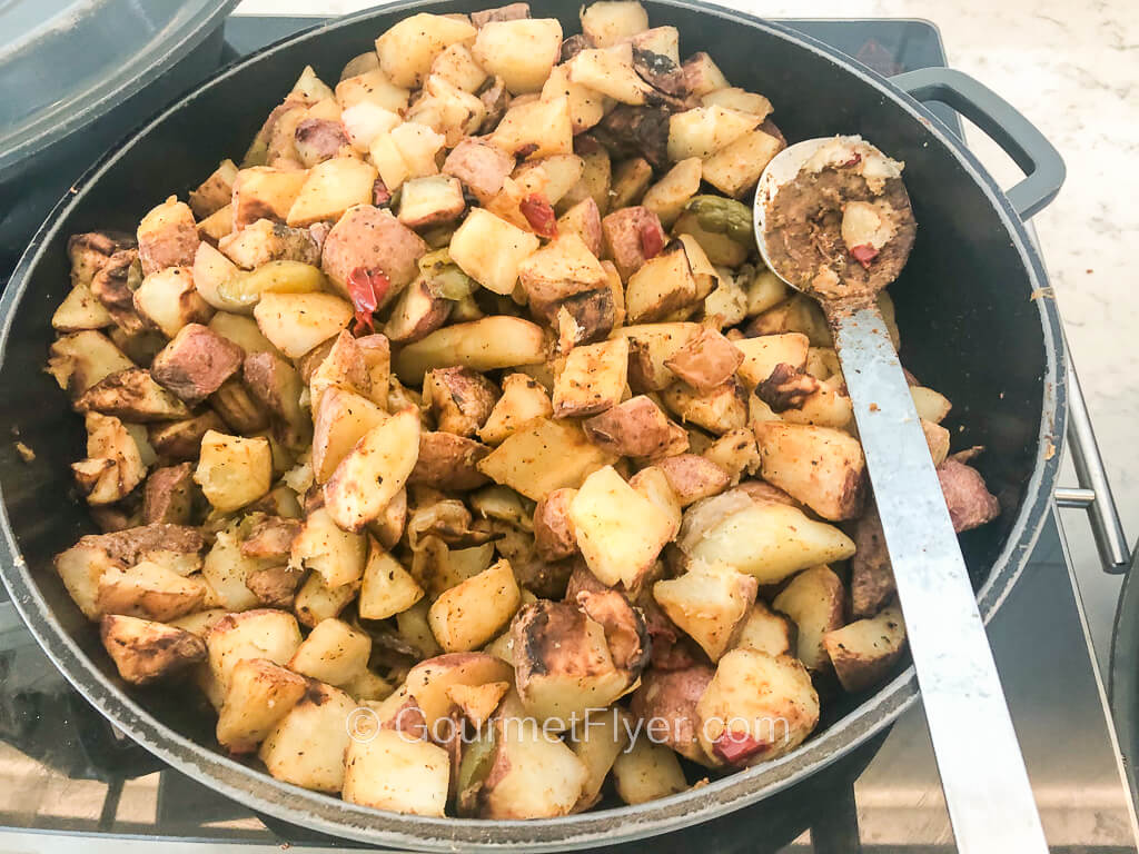 A round cast iron platter on a heating element is filled with diced and sauteed redskin potatoes.