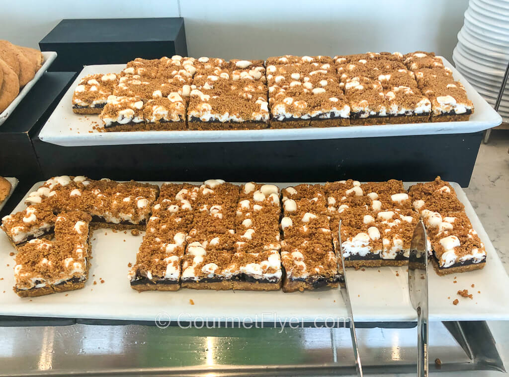 Two long platters, one on top of the other, is filed with a dessert where a piece of marshmallow is sandwiched between two thin biscuits.