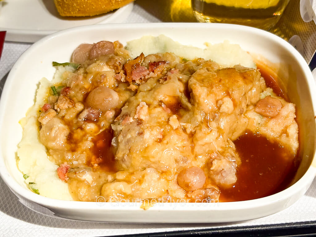 A dish with chicken meat in a brown sauce sitting on a layer of mashed potatoes.