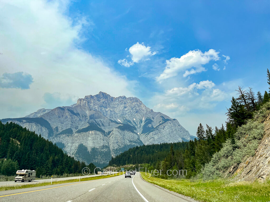 A four-lane divided highway has a majestic mountain in its backdrop under sunny blue skies.