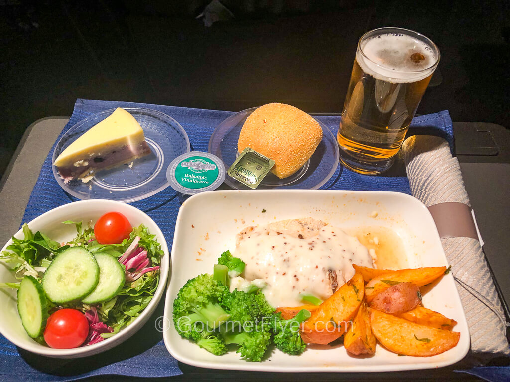 A dinner tray contains plates of food including a chicken dish and a green salad accompanied by a glass of beer.