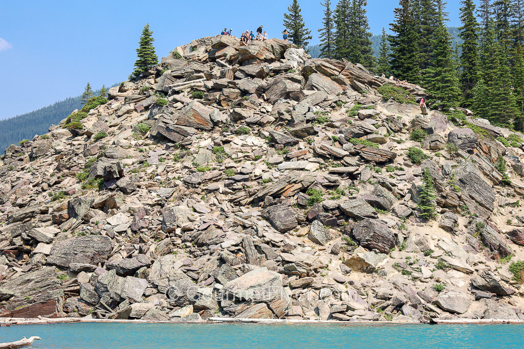 Hikers are seen on top of a hill composed of a pile of rocks.