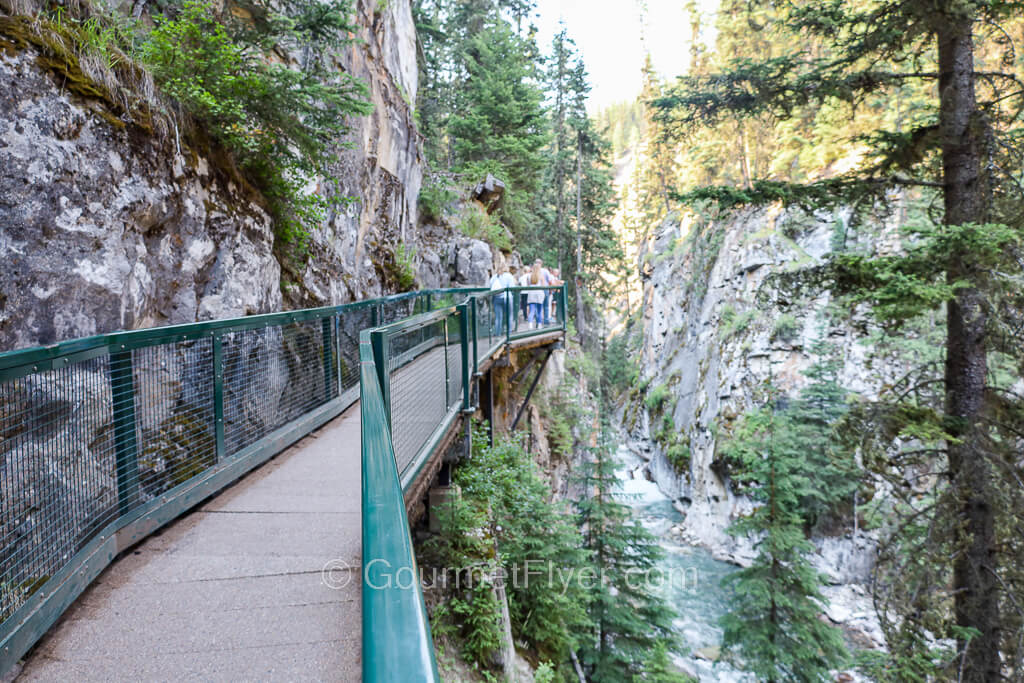 A concrete bridge path is built alongside the mountain on the left and above a creek to the right.