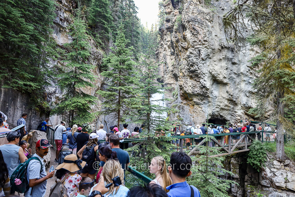 People line up against a fence leading to a waterfall and a small opening to a cave.