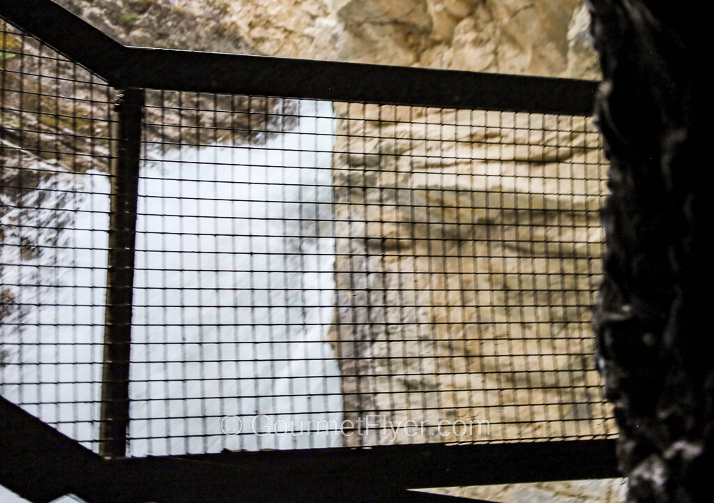 The end of a path leading to a waterfall is blocked by a tall and black metal fence.