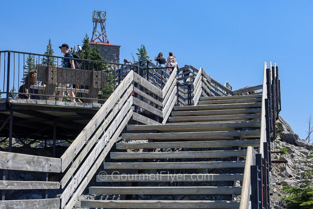 Tourists walk up a series of wooden staircases leading to an antenna structure at the peak.