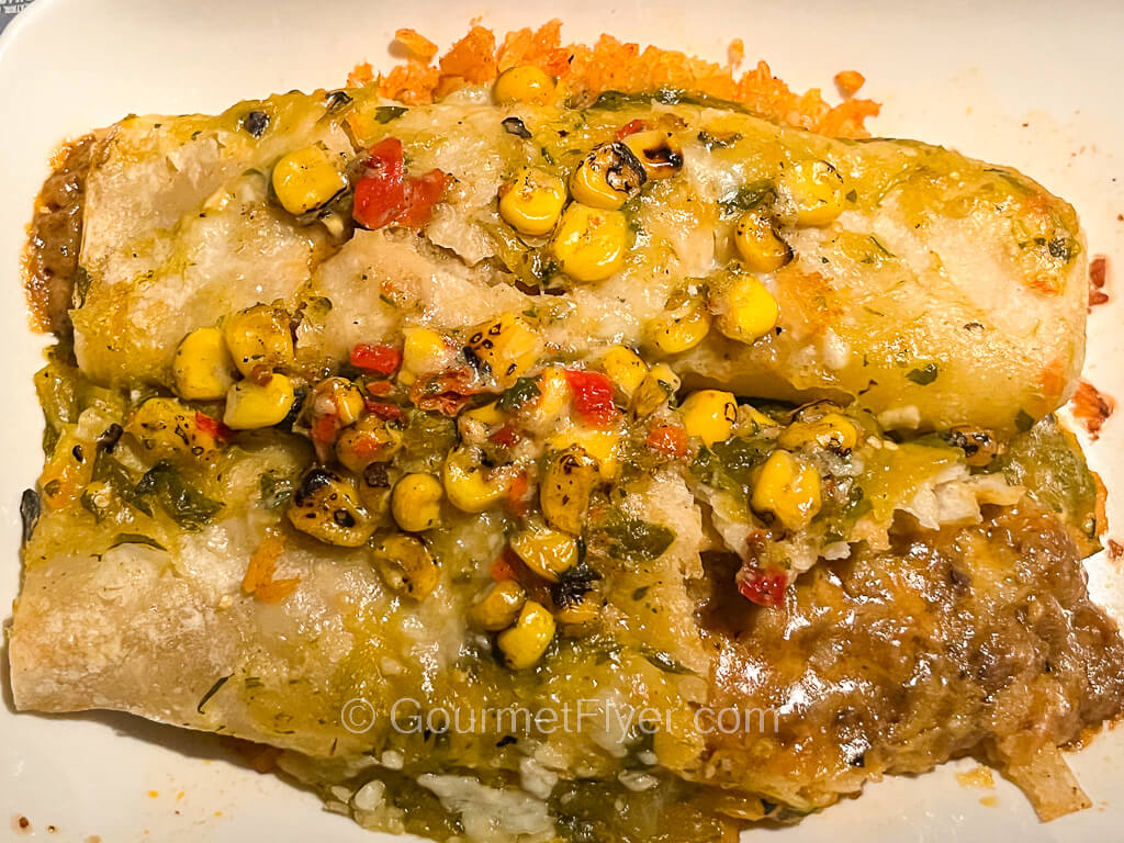 A pair of enchiladas are served on a plate and topped with corn and sauce.