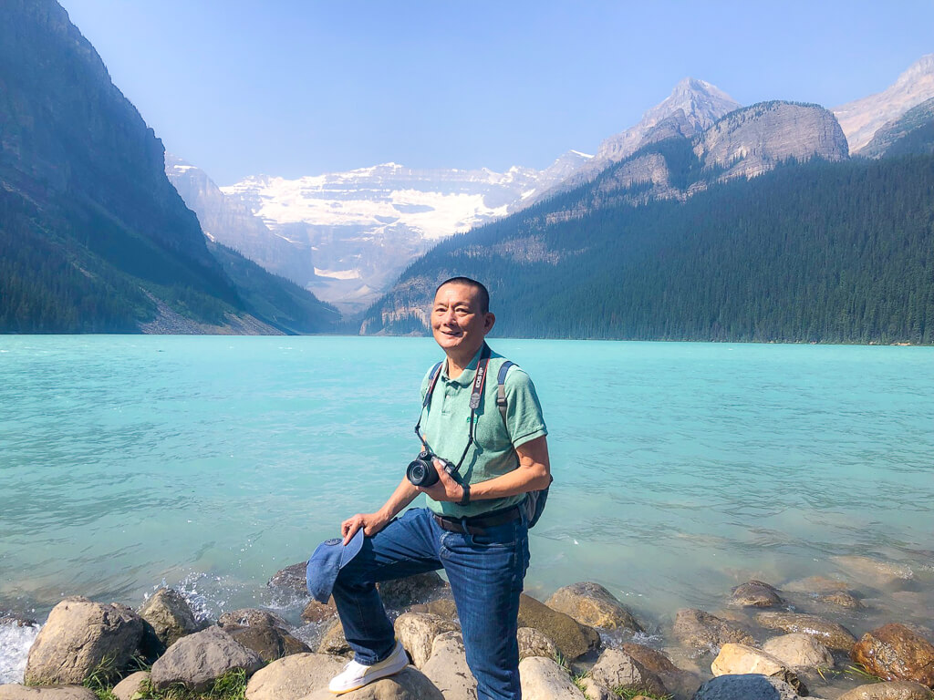 The Gourmet Flyer is posing in front of a lake with a glacier mountain in the background.