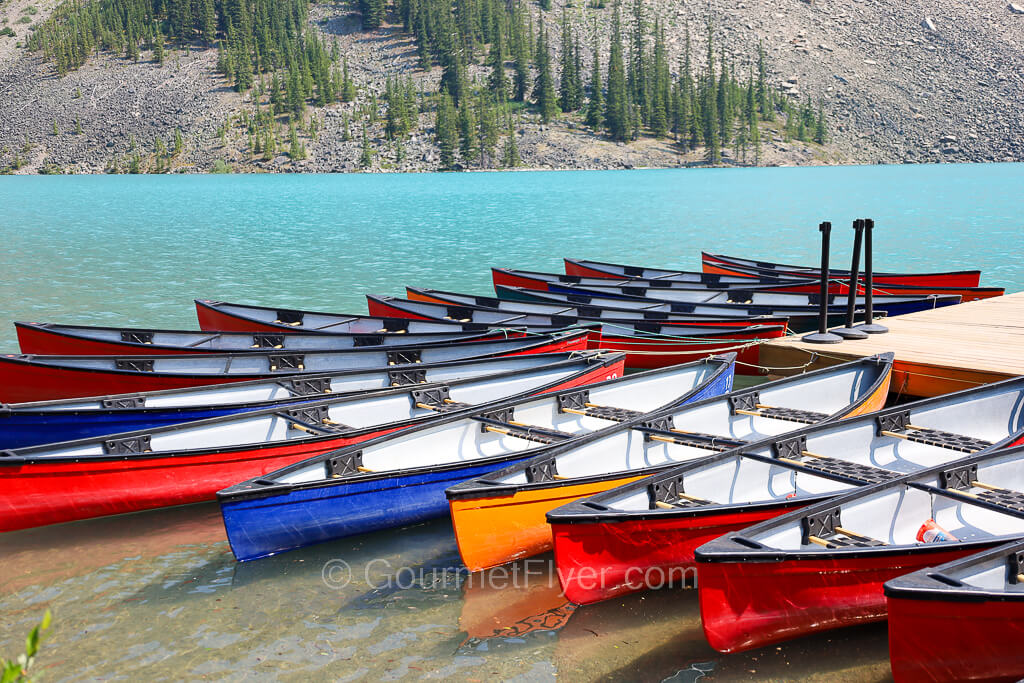 An array of colorful canoes is parked on the edge of a lake with turquoise water.